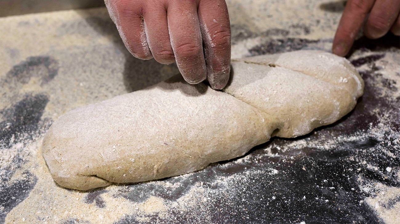 Mani che lavorano un impasto sul banco infarinato del forno Mulinum